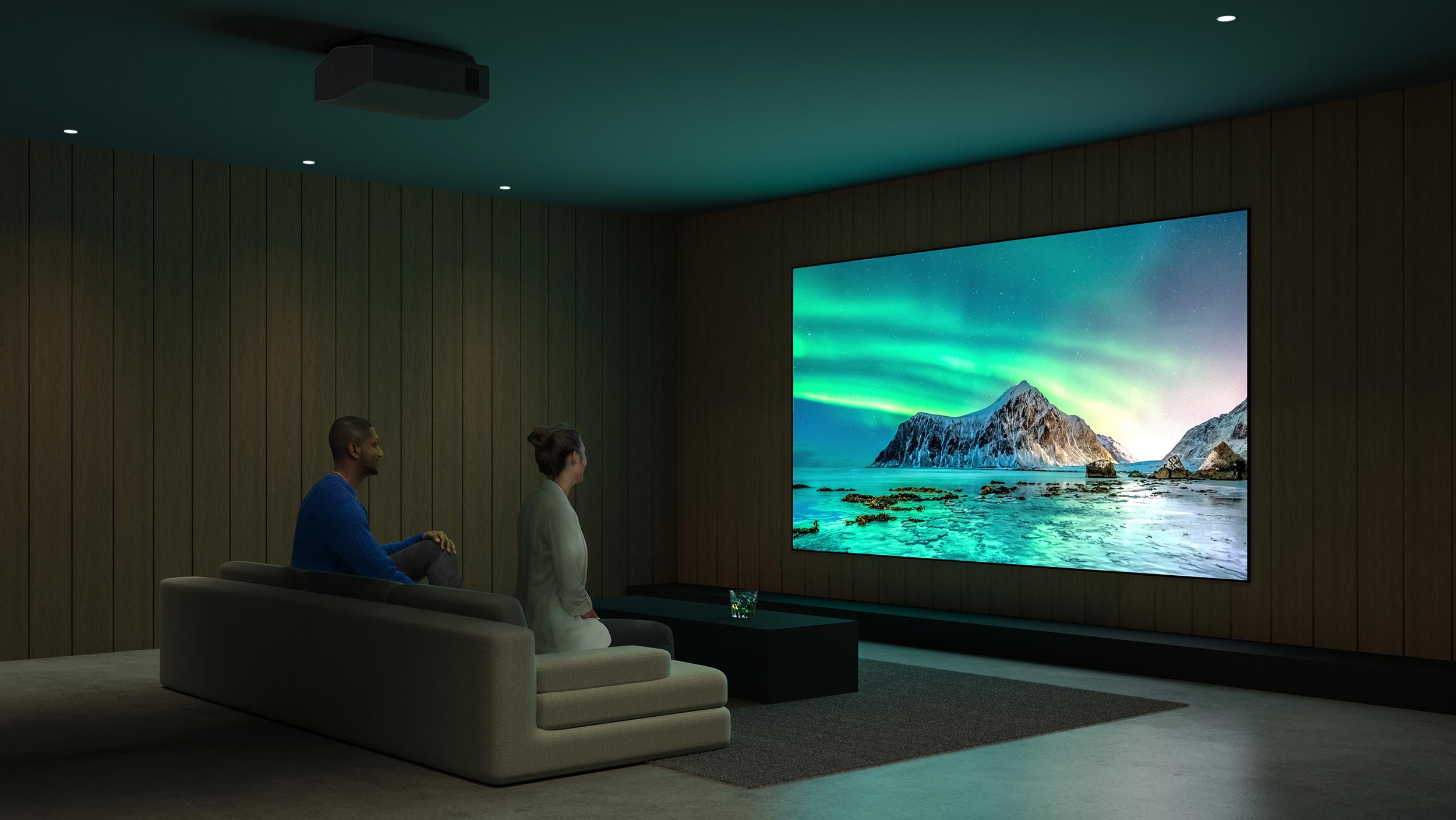 Two people sitting on a couch in a dark room, watching a large screen displaying a scenic mountain view.